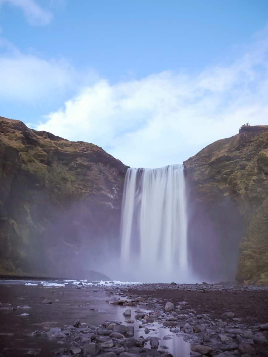 Premium Photo  A rock formation appears to gaze in silence at the imposing  skogafoss waterfall during an evening icelandic summer